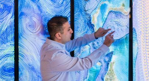 埃罗尔·艾加尔在达勒姆的海岸和海洋测绘中心进行数据可视化研究，他的硕士论文使用了一个巨大的彩色屏幕墙壁投影.